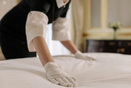 A housekeeper straightening the bed linens in a well-appointed hotel room.